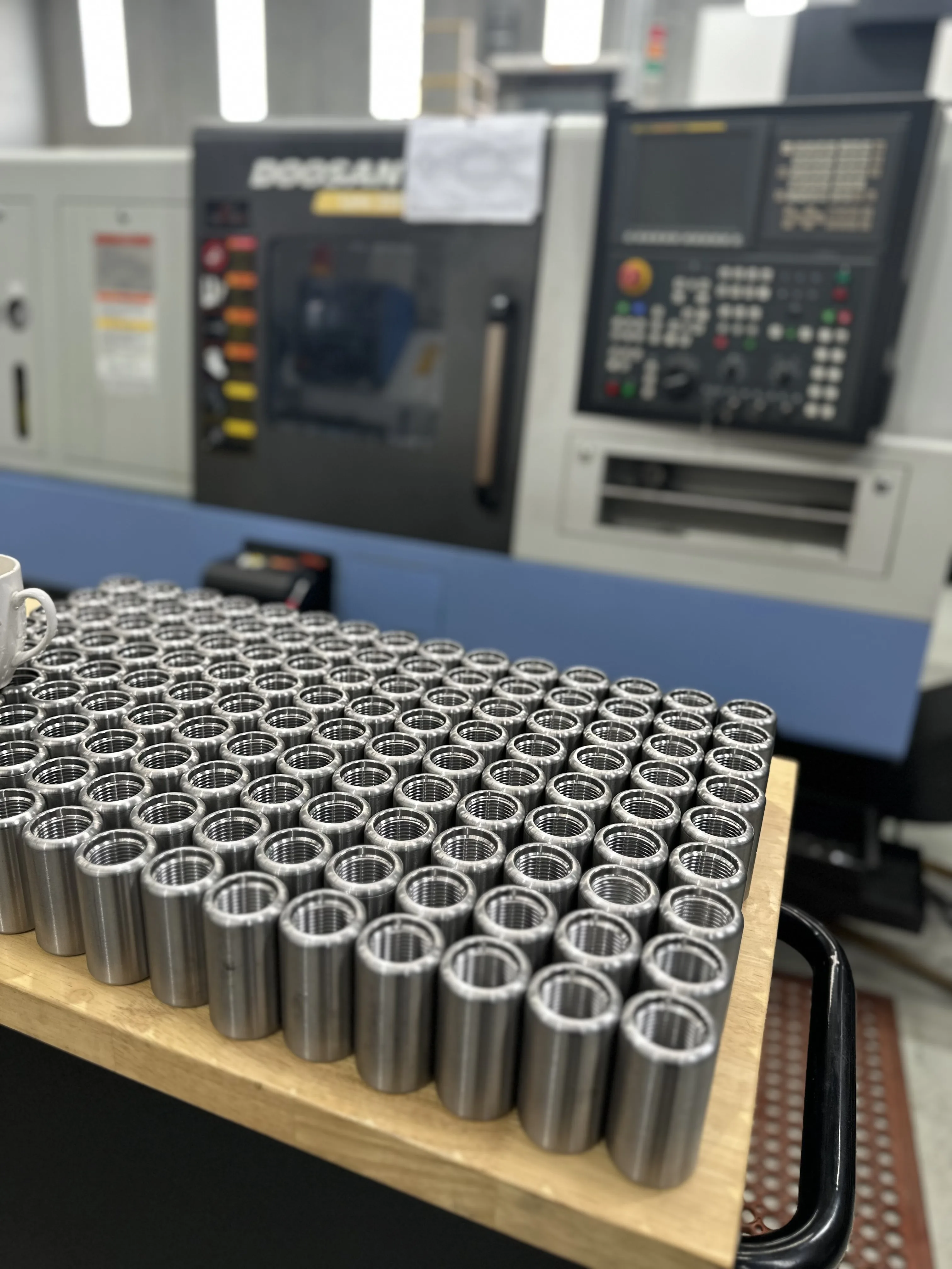 Production batch of turned steel bushings, Doosan CNC lathe behind, Padco Engineering